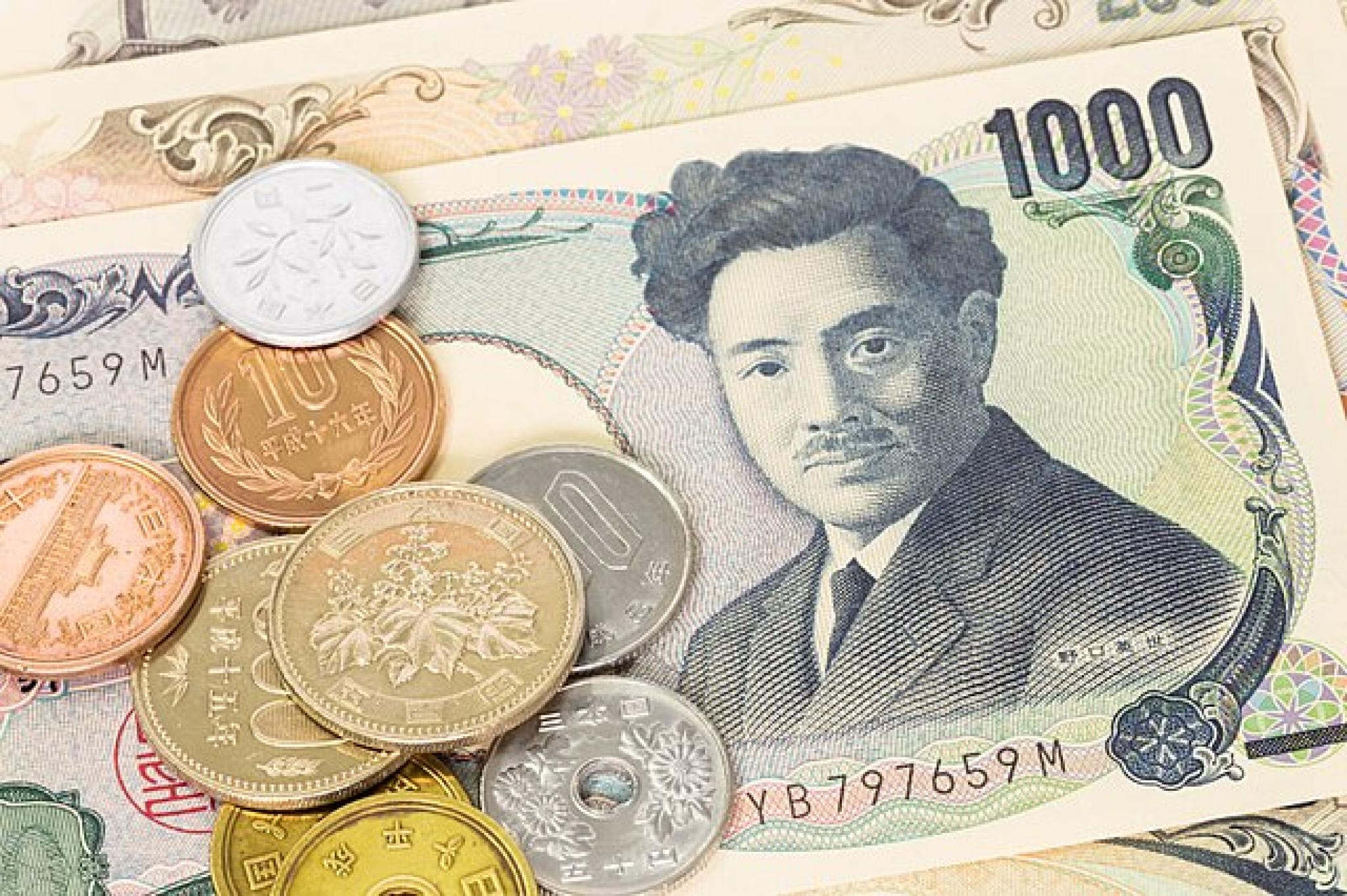 A collection of Japanese yen banknotes and coins. A 1,000 yen note featuring a portrait of Natsume Sōseki is prominently displayed, with various yen coins of different denominations, including 1, 5, 10, 50, 100, and 500 yen, scattered on top.