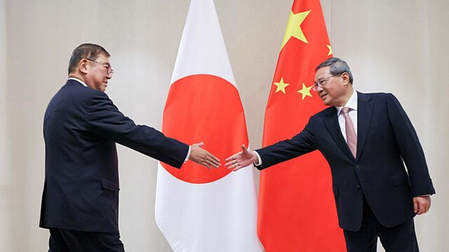 Japanese and Chinese Leaders Meet for Diplomatic Talks in Vientiane (2024) Japanese politician Shigeru Ishiba and Chinese Premier Li Qiang extend hands for a handshake during a diplomatic meeting, standing in front of the national flags of Japan and China.